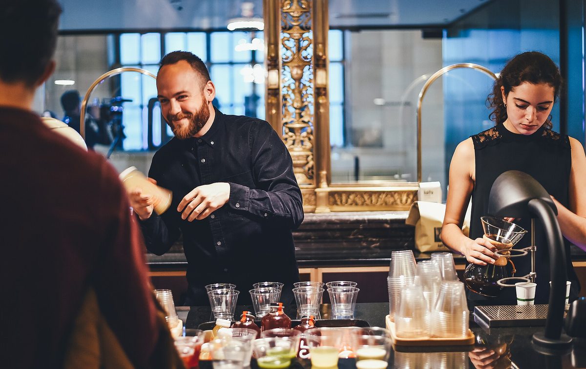 A bartender shaking a cocktail behind a bar lined with bottles and glasses