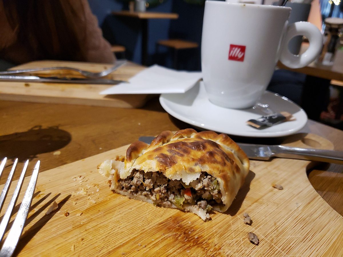 Cross-section of an Argentine beef empanada showing the juicy filling, beside a cup of coffee