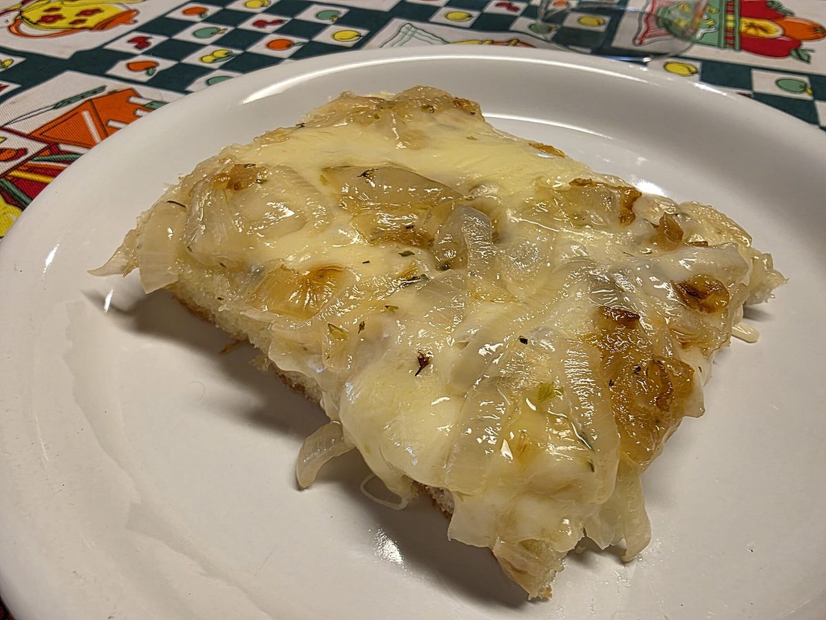 A thick slice of Argentine fugazzeta pizza loaded with melted cheese and sweet onions