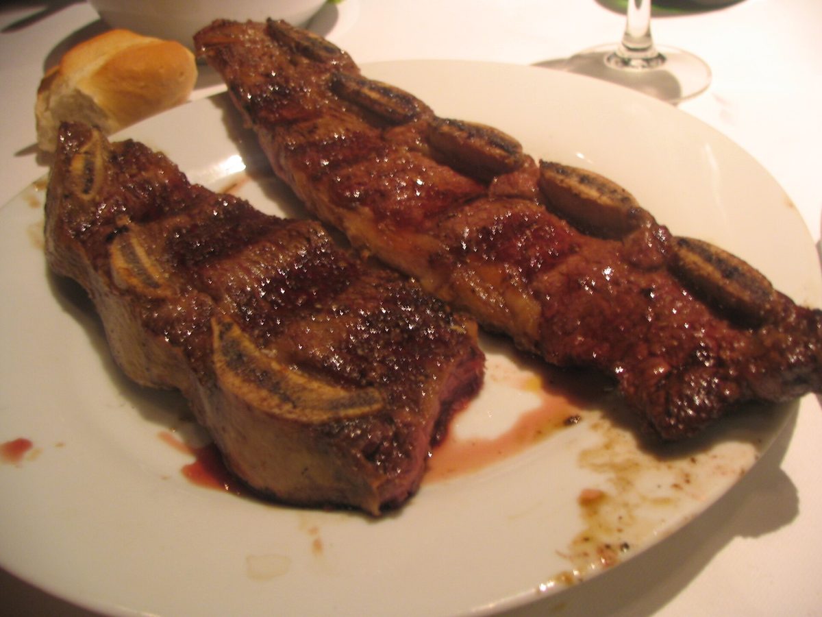 Grilled tira de asado short ribs on a plate with bread and wine, the classic Recoleta parrilla experience