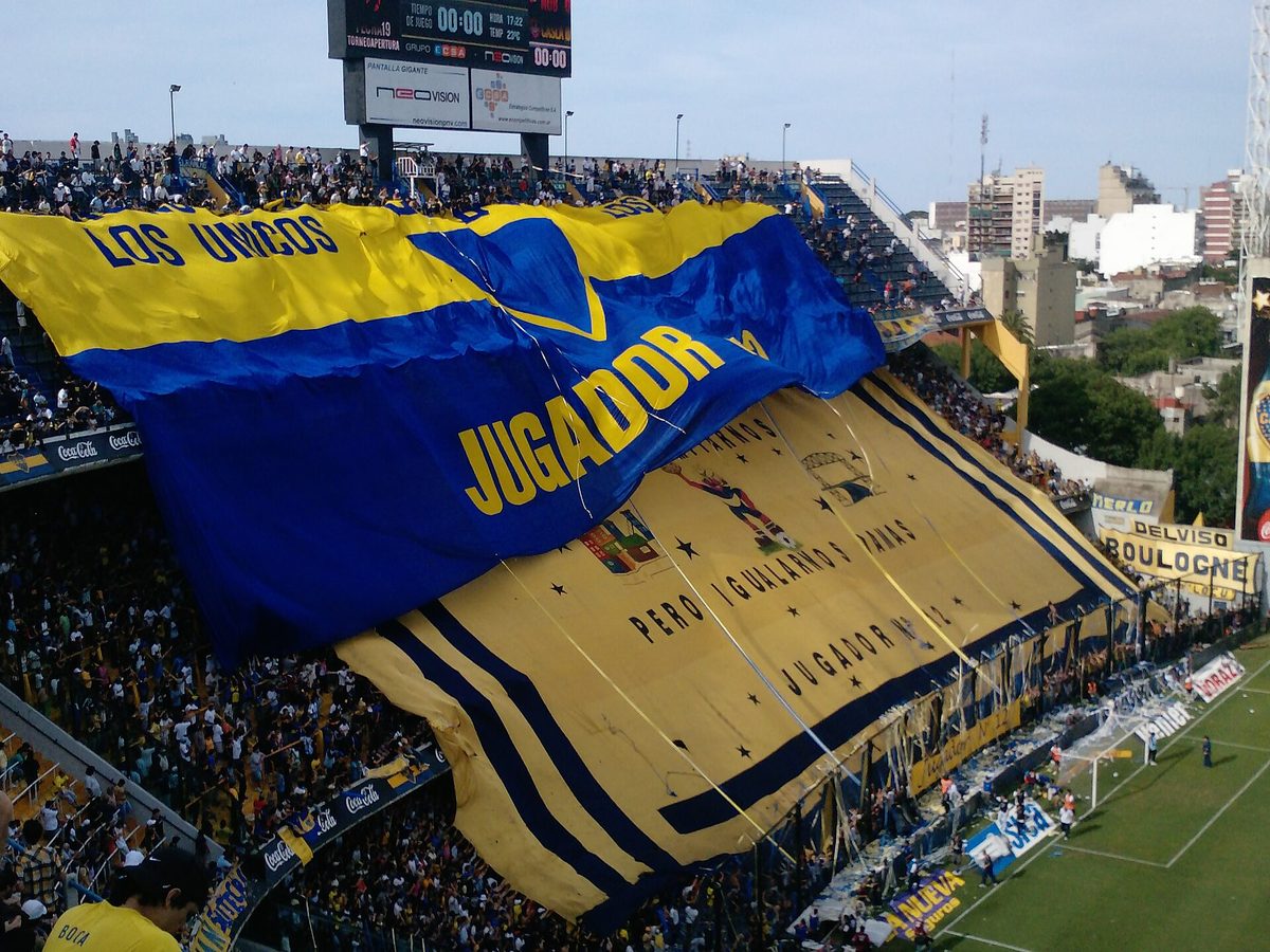 Boca Juniors hinchada unfurling a giant blue and gold flag across the stands of La Bombonera