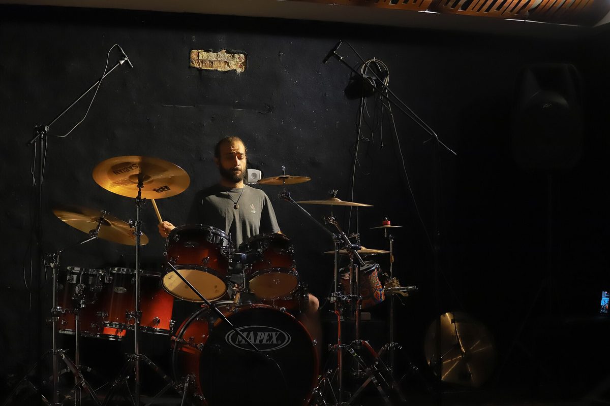 Drummer behind a full kit in a dark intimate venue, evoking La Bomba de Tiempo at Konex