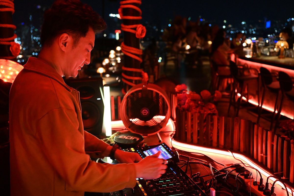 A DJ plays a rooftop bar at night with city lights glittering below, the kind of high-up scene rooftop bars deliver