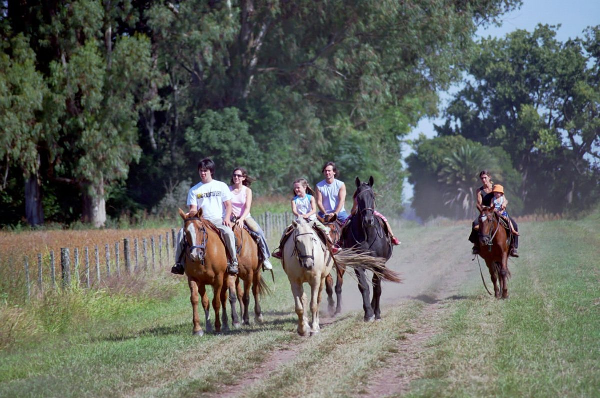 A family on horseback rides a tree-lined country lane at a pampas estancia near Buenos Aires