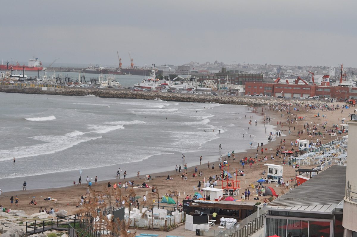 A busy beach with surf and the fishing port behind on a mar del plata day trip from buenos aires