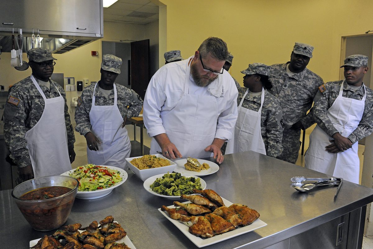 A chef in whites plating dishes on a kitchen counter, as a closed-door host would before service