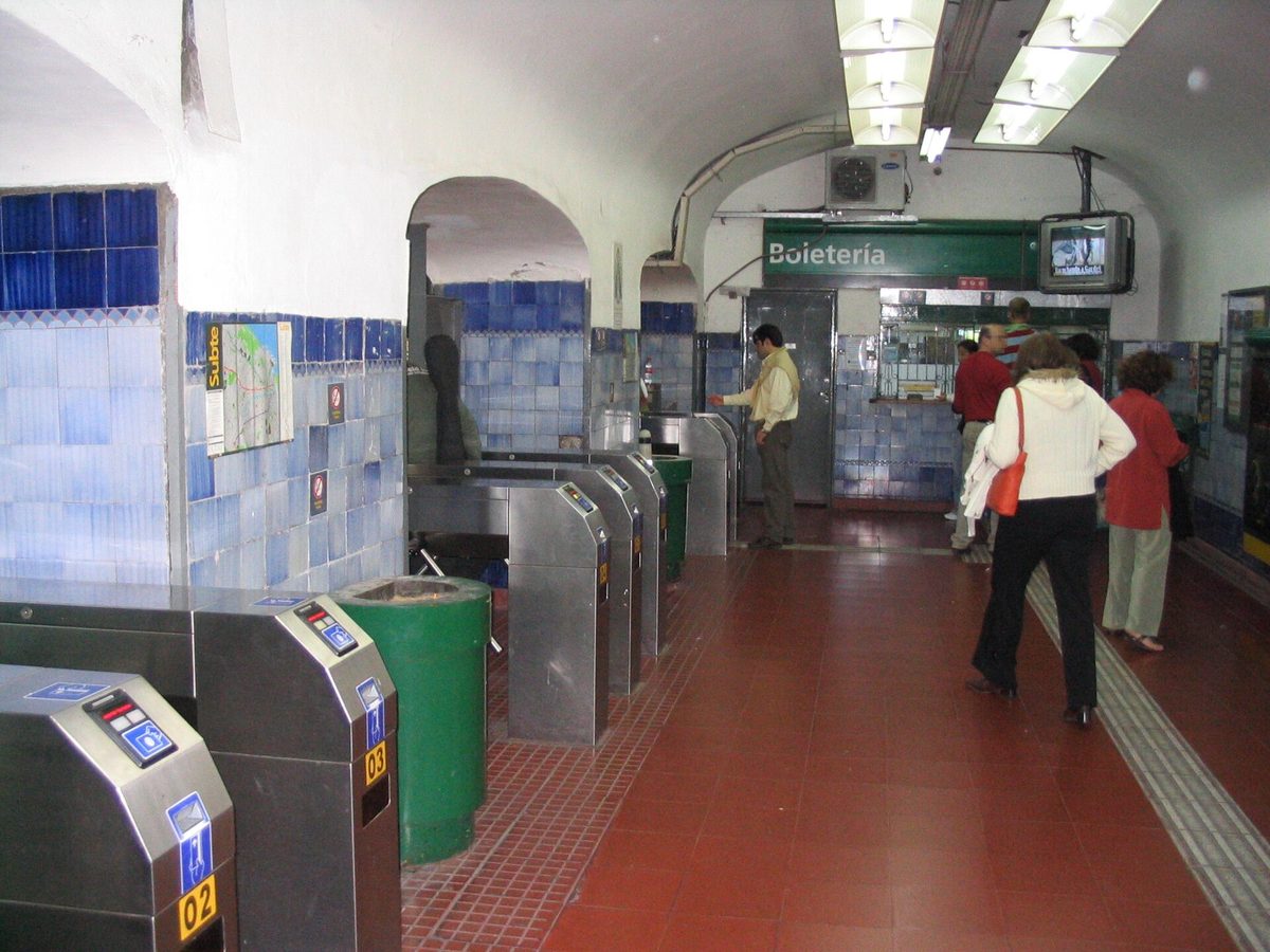 Turnstiles and ticket booth inside a Buenos Aires Subte station where you tap a SUBE card to enter