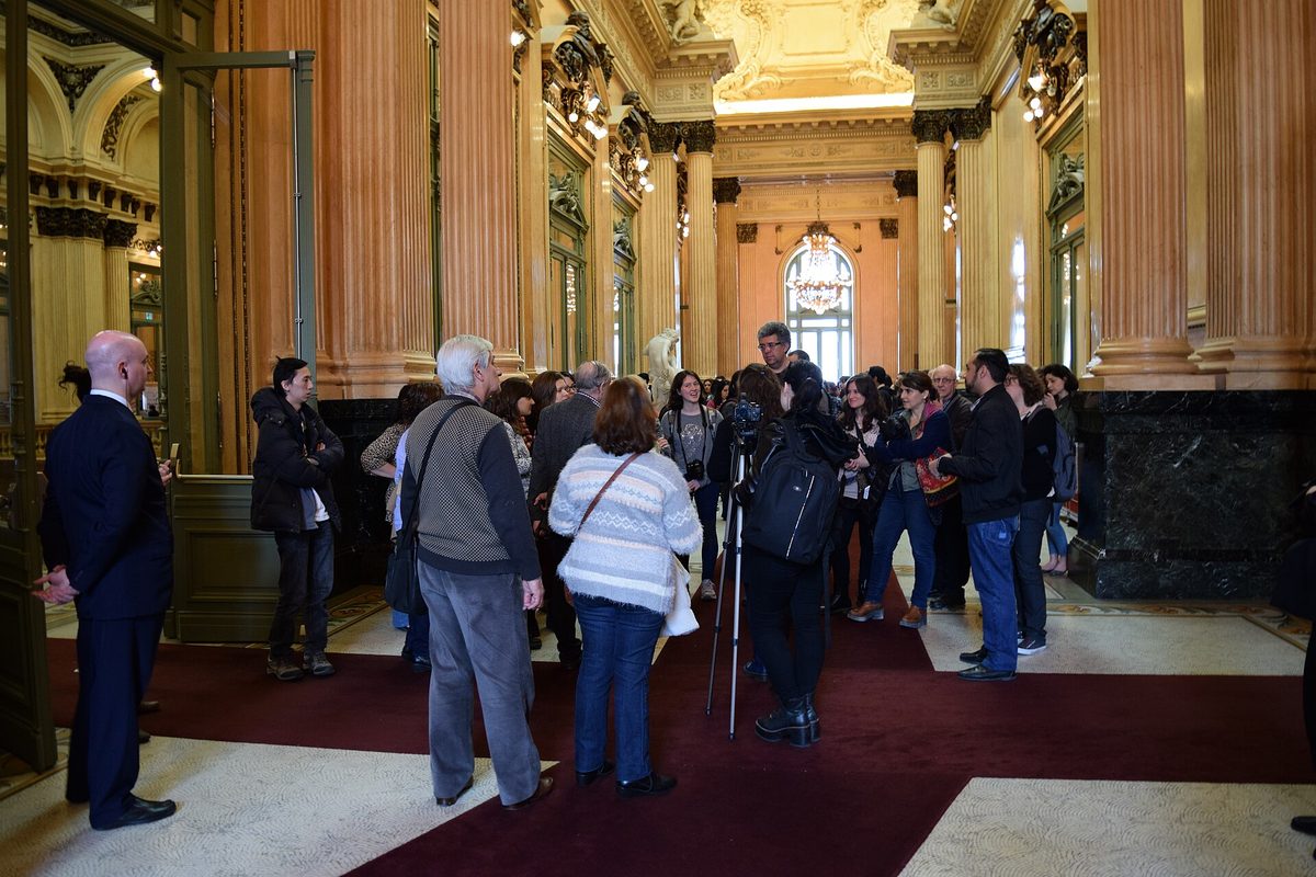A guided-tour group gathered in the marble-columned entrance foyer of the Teatro Colon
