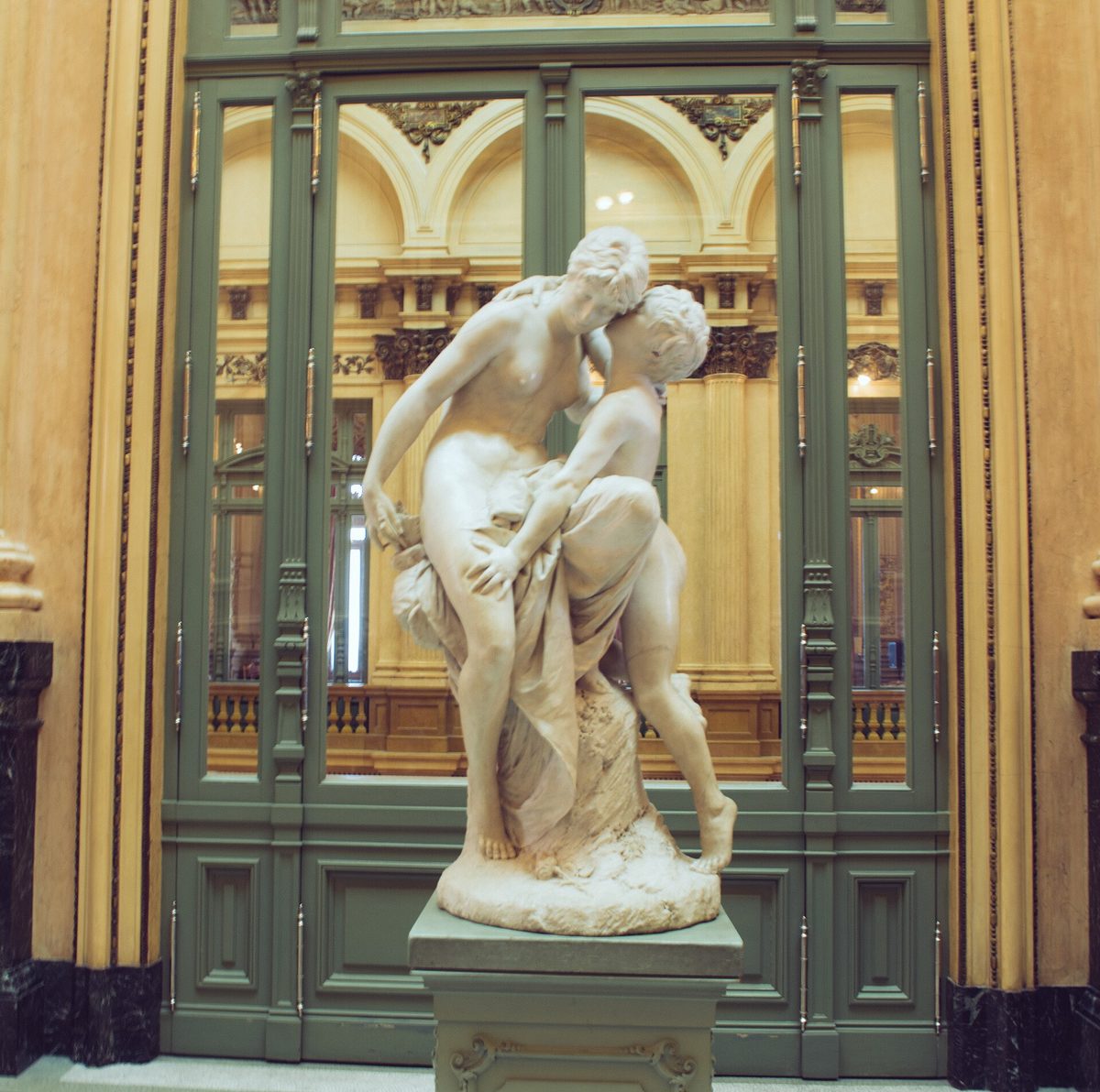 A marble sculpture set against gilded balustrades in an ornate interior gallery of the Teatro Colon