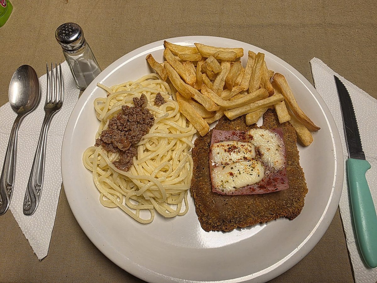 Argentine milanesa napolitana, a breaded beef cutlet topped with ham and melted cheese, served with fries and pasta