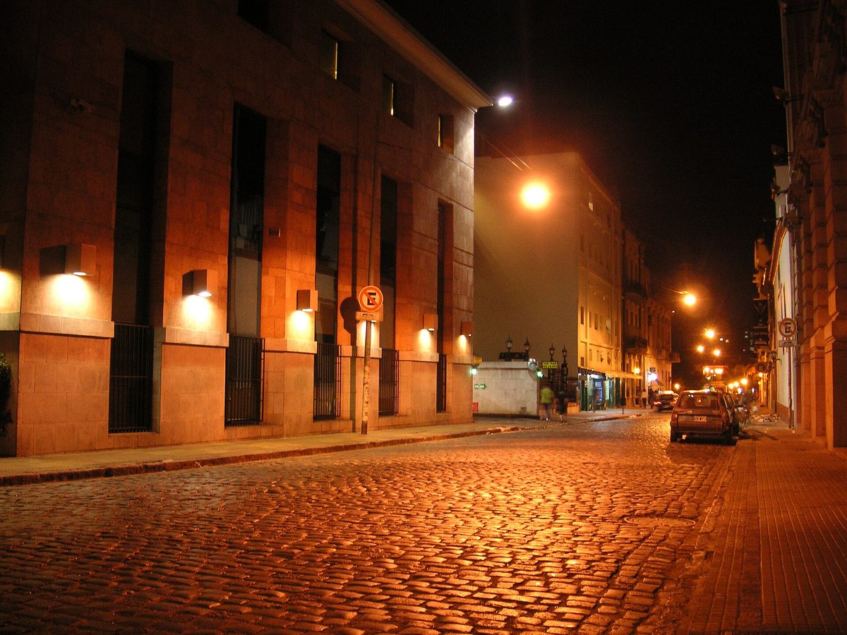 A cobbled San Telmo street in Buenos Aires lit up at night, lined with the barrio's bohemian bars and tango haunts